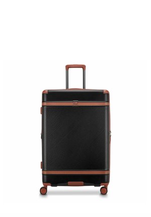 Valigia rigida nera con rifiniture marroni, quattro ruote e manico telescopico sollevato, in piedi su sfondo bianco.