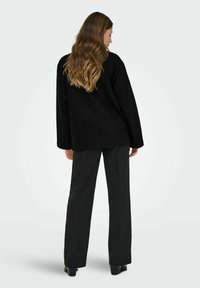 Veste noire surdimensionnée avec une silhouette droite et des manches longues, associée à un pantalon noir ajusté. Texture lisse, design minimaliste.