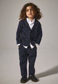 Marineblau kariertes Blazer- und Hosen-Set, weißes Hemd darunter, mit Revers und zwei Vorder Taschen, kombiniert mit schwarzen Schuhen.