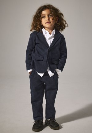 Marineblau kariertes Blazer- und Hosen-Set, weißes Hemd darunter, mit Revers und zwei Vorder Taschen, kombiniert mit schwarzen Schuhen.