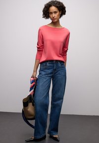 Pull à manches longues corail, jean ample bleu, ballerines noires. Porte un sac marron avec un accent noir et une écharpe multicolore.