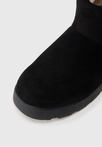Černé semišové kotníkové boty s kulatou špičkou a měkkou vnitřní podšívkou. Mají silnou černou gumovou podrážku pro podporu a trakci.