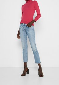 Aangesloten roze coltrui, lichtblauwe rechte jeans met een onafgewerkte zoom, gecombineerd met zwarte haksandalen. Glad materiaal en casual ontwerp.
