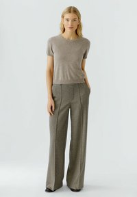 Beige Kurzarmstrickoberteil mit verziertem Ausschnitt, kombiniert mit weit geschnittenen karierter Hose. Die Hose hat ein Hahnentritt-Muster und vordere Taschen.