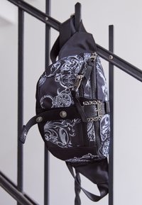 Black bag with a white floral pattern, featuring zippers and metal accents. Made from fabric with a textured look; adjustable strap.
