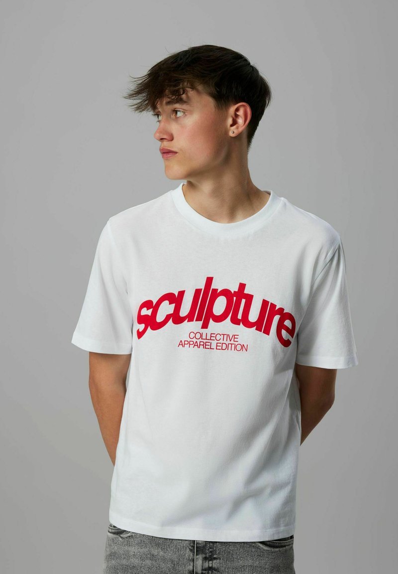 Vit bomulls t-shirt med korta ärmar, med fet röd text som står "sculpture COLLECTIVE APPAREL EDITION" över framsidan.