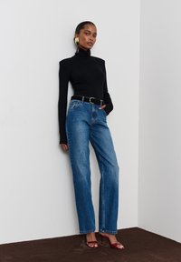 Fekete bordázott garbó, magas derekú, egyenes szárú kék farmernadrág, fekete övvel megkötve, piros magassarkú szandálokkal párosítva.