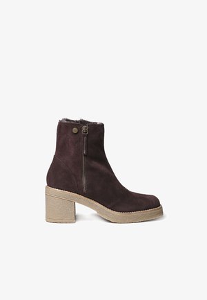 Dark brown suede ankle boot with a chunky heel, side zipper, and soft faux fur lining at the top. Noticeable textured sole for grip.