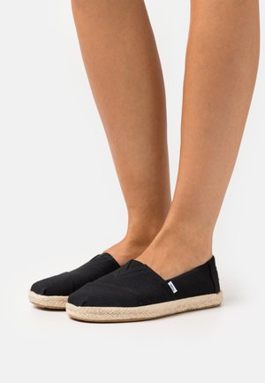 Black canvas espadrilles with a woven jute sole, featuring a slip-on design and stitched detailing along the vamp. Minimal branding visible.