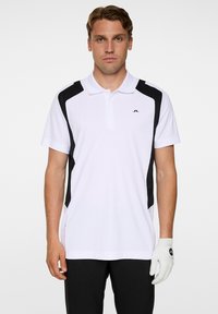 Vit herrpolo med svarta sidopaneler, korta ärmar och krage. Har en logotyp på bröstet. Slät tygtextur.