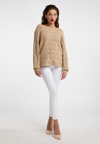 Pulover bej din tricotaj cu un croi lejer și gât larg, purtat cu blugi skinny albi și tocuri bej. Material texturat și mâneci lungi.
