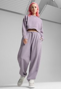 Sudadera corta de color púrpura claro con cuello redondo y puños acanalados, combinada con pantalones de chándal holgados de color púrpura claro. Zapatillas blancas abajo.