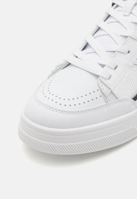 Sneaker alb cu un superior din piele netedă, cutie de degete perforată, șireturi plate albe și talpă din cauciuc nervurată. Design minimalist cu accente subtile.