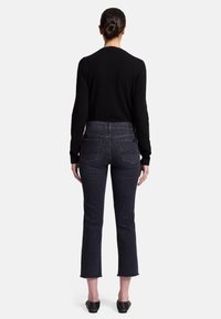 Haut noir à manches longues et jeans en denim sombre avec un ourlet court et des bords effilochés, dotés de poches arrière et d'une silhouette ajustée.