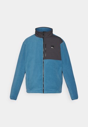 Chaqueta de forro polar en azul con acentos en negro. Presenta un cuello alto, cremallera frontal y un bolsillo en la parte superior izquierda con un logotipo. Textura suave.