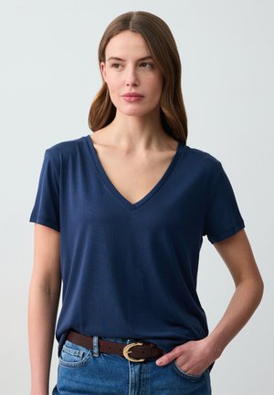 Maglietta V-neck blu navy in tessuto morbido, maniche corte, vestibilità comoda, abbinata a una cintura marrone con fibbia dorata, indossata con jeans blu.