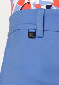 Pantaloni blu in tessuto testurizzato con frontale piatto. Presentano un logo RL argento sulla vita. Linee pulite e vestibilità sartoriale.