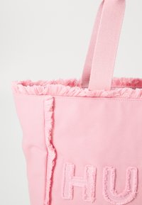 Roze canvas tas met rafelige randen, voorzien van gestikte letters. De tas heeft een eenvoudig ontwerp en stevige stoffen hengsels.