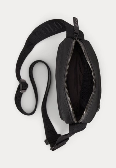 Black crossbody bag with partially open zipper showing empty interior and adjustable strap with buckle on plain light background.