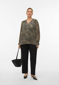 Blouse à manches longues noire et dorée avec un col en V, présentant un motif à rayures ondulées, assortie à un pantalon noir à jambe droite et un sac à main noir.