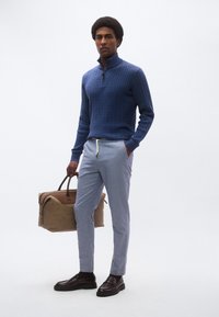 Μπλε πουλόβερ με πλέξη καλώδιο και ψηλό γιακά, ανοιχτό μπλε παντελόνι με κορδόνι, καφέ τσάντα και σκούρα καφέ παπούτσια. Ομαλή υφή, casual εφαρμογή.