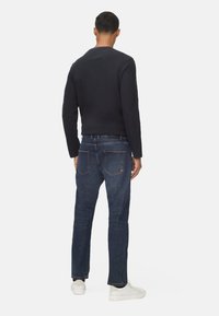 Marineblauwe crewneck trui gecombineerd met donkerblauwe jeans. De trui heeft een gladde textuur, en de jeans hebben twee achterzakken en subtiele stiksels.