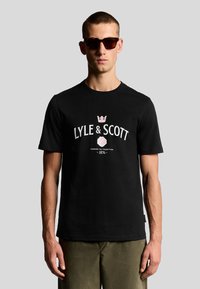 Camiseta de algodón negra con cuello redondo, que presenta un texto de logo impreso en blanco y rosa con un diseño de corona y rosa en el centro.