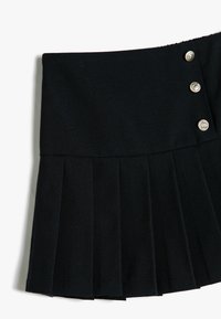 Zwarte geplooide rok met een gladde tailleband, voorzien van drie decoratieve zilveren knopen aan één kant. Gemaakt van zachte stof met een gestructureerde afwerking.