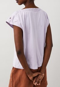 Kratší rukáv levandulové tričko s krajkovým detailem podél výstřihu. Měkká tkanina s volným střihem, spárované s oranžovo-hnědou sukní.