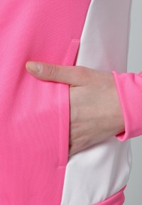 Main insérée dans la poche latérale d'un vêtement rose et blanc avec une longue manche rose visible.