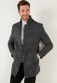 Abrigo de cuadros gris con cuello alto, cierre de botones y bolsillos laterales. Fabricado en tejido texturizado, con un corte estructurado y forro en contraste.