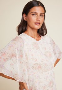 Blomstrete kjole i lett stoff, med korte, flytende ermer, rund utringning og en pastellfargepalett med rosa og beige mønstre.
