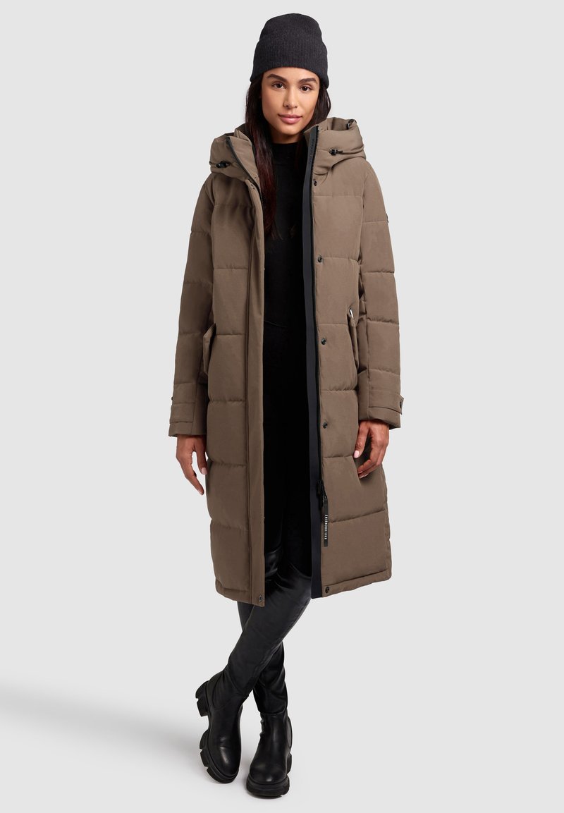 Brauner gepolsterter langer Mantel mit Kapuze, ausgestattet mit einem Reißverschluss und Druckknopfverschluss, seitlichen Taschen und einer glatten Textur. Trägt man über einem schwarzen Outfit.