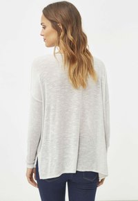 Suéter de color gris claro, de corte holgado, con mangas largas y un dobladillo relajado. La tela de punto texturizada tiene una apariencia suave y semi-translúcida.