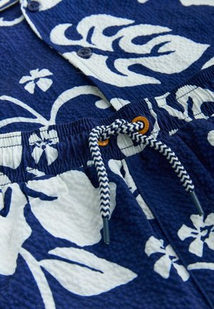 Dunkelblaues Hemd mit weißem Blumenmuster; strukturierter Stoff; mit Knöpfen und einem elastischen Bund mit geflochtenem Kordelzug.