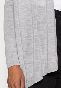 Ljusgrå kardiagan gjord av mjukt, lättviktigt material. Har en lös passform, långa ärmar och ribbat trim längs nederkanten.