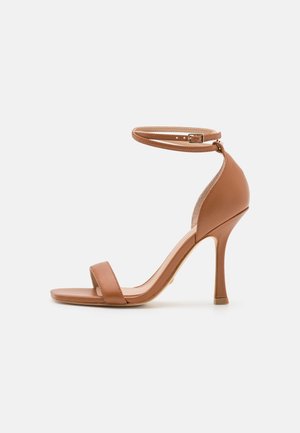 Las sandalias de tacón alto de cuero marrón cuentan con una delgada correa en el tobillo, puntera abierta y un acabado suave y mate. El tacón mide aproximadamente 10 centímetros de alto.