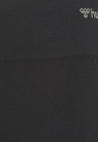 Zwarte leggings van een gladde, textuurstof. Voorzien van een brede tailleband en een klein logo aan de bovenkant in een contrasterende kleur.