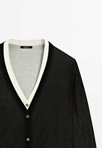 Cardigan noir avec bordure blanche le long du col en V et fermeture par boutons, en tissu tricoté léger, manches longues.