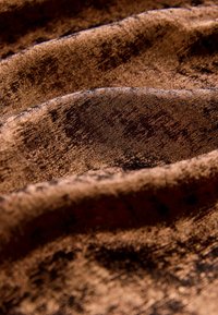 Pomarszczony materiał w bogatych odcieniach brązu, o teksturze z delikatnym połyskiem. Powierzchnia ukazuje wzór z różnymi odcieniami i refleksami.