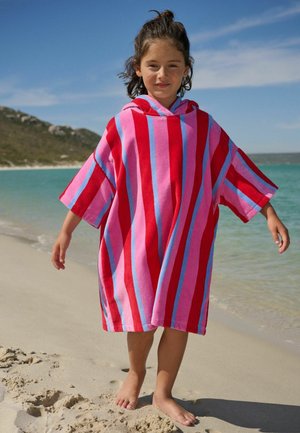 Kind steht barfuß am Sandstrand und trägt einen Kapuzenhandtuch-Poncho mit roten, pinken und blauen Streifen nahe dem ruhigen Meer.