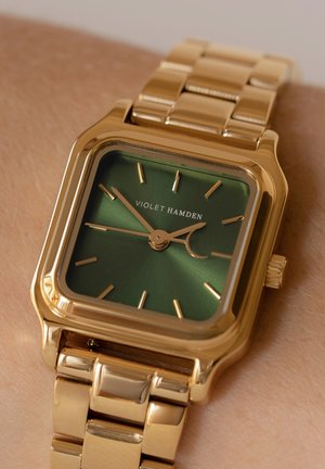Montre rectangulaire dorée avec un cadran vert, comportant des index et aiguilles dorés. Le bracelet en métal à maillons complète l'ensemble du design.