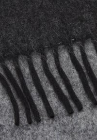 Écharpe en laine noire avec bord à franges, présentant une texture douce et un dégradé du noir foncé au gris clair. Design finement tissé.