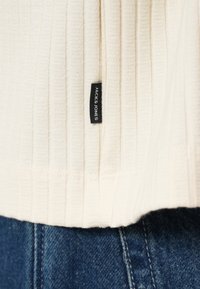 Υφασμα με ριγέ κρέμα χρώμα και μικρή μαύρη ταμπέλα "Jack & Jones" πάνω από το ράψιμο των μπλε τζιν.