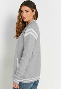 Grijze sweatshirt met witte strepen op de schouders en mouwen, voorzien van een ritssluiting aan de voorkant en zijzakken. Gemaakt van een zachte, gestructureerde stof.