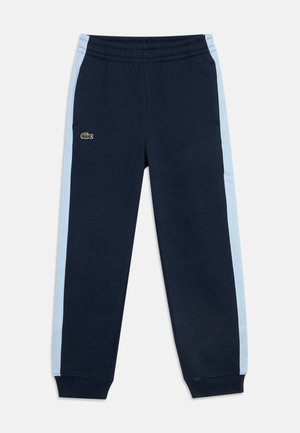Pantalon de survêtement bleu marine avec des bandes latérales bleu clair, taille élastique, poignets côtelés aux chevilles et un petit logo crocodile vert sur la cuisse gauche.