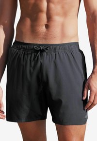 Schwarze Badeshorts mit elastischem Bund und Kordelzug. Hergestellt aus leichtem Material, mit Seitentaschen und kleinem Logo am Saum.