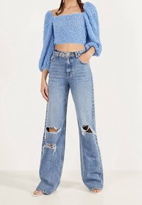 Modrý strukturovaný zkrácený top s nafouknutými rukávy, skombinovaný s světle modrými džíny s vysokým pasem a širokými nohavicemi, které mají velké trhliny na kolenou.