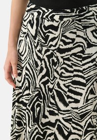 Jupe à rayures zèbre noir et blanc en tissu doux, avec une taille élastique et un design fluide. Gros plan sur une main tenant la jupe.