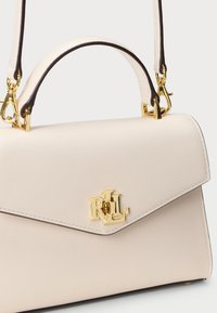 Μπεζ δερμάτινη τσάντα χειρός με δομημένο σχήμα, διαθέτει κούμπωμα με χρυσό λογότυπο και αντίθετες σκούρες δερμάτινες λεπτομέρειες στ η λαβή.